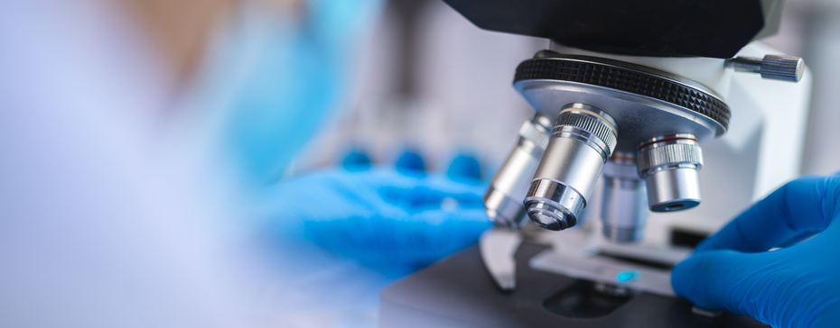 Mikroskop u laboratoriji s rukama osobe koja nosi plave rukavice, pažljivo podešavajući sočiva. Fokus je na mikroskopu dok se istraživač priprema za analizu uzoraka.